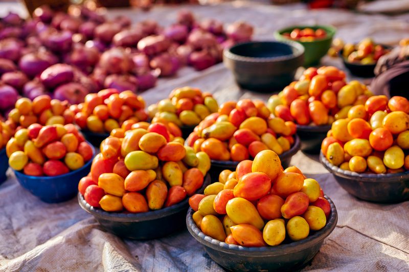 Bowls of colourful tomatoes and shallots laid out on a market cloth