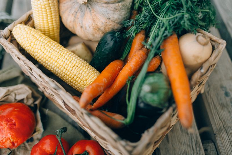 A wicker basket of carrots, sweetcorn, tomatoes and leafy greens