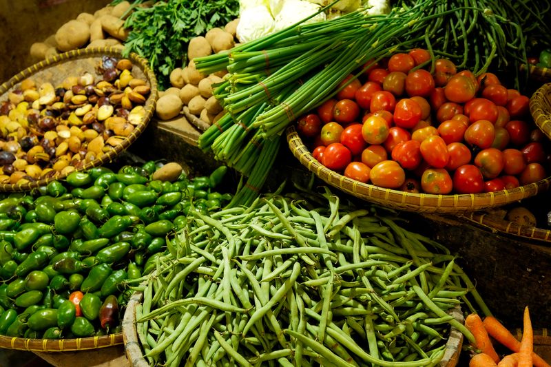 A market stall of green beans, tomatoes, spring onions and avocados in woven baskets