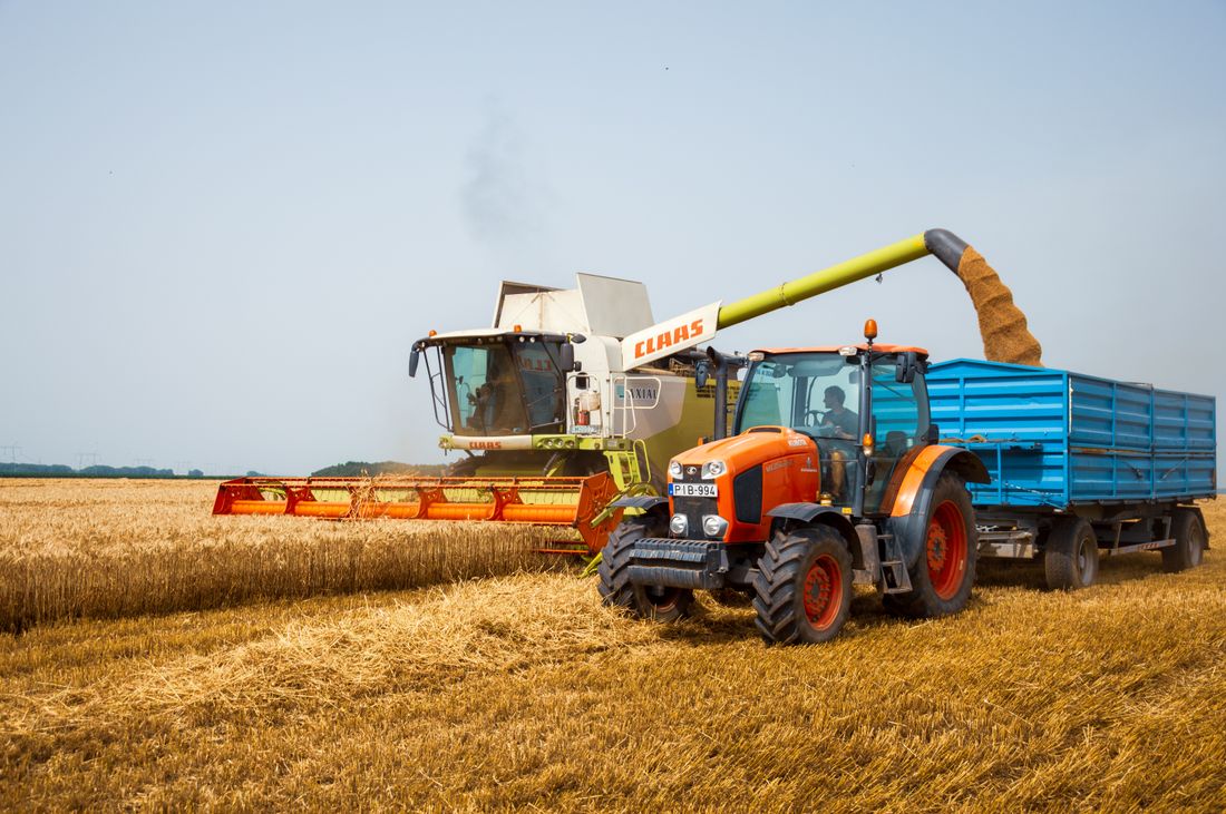 A combine harvester unloading grain into a trailer pulled by an orange tractor