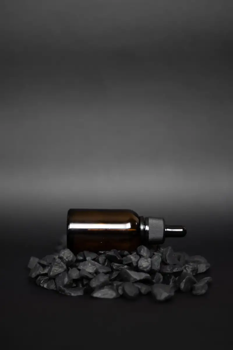 An amber dropper bottle resting on dark stones against a grey-to-black seamless backdrop