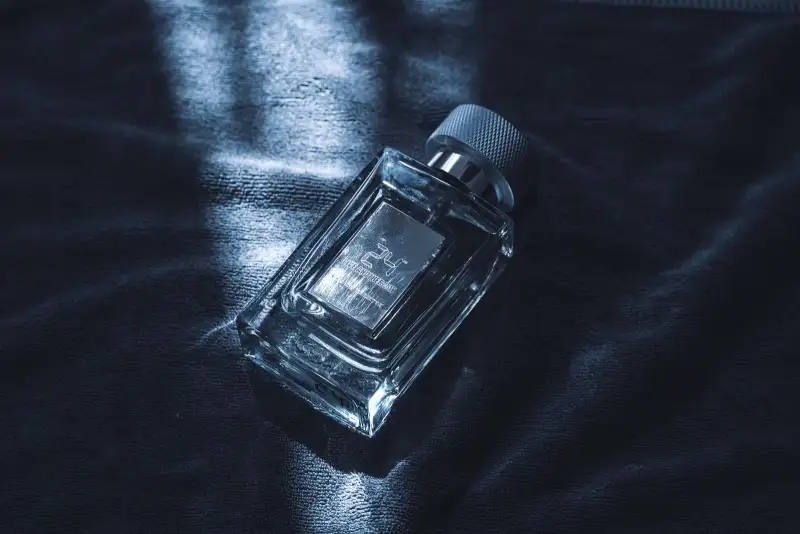 A glass perfume bottle lying on dark velvet with stripes of cool light across it