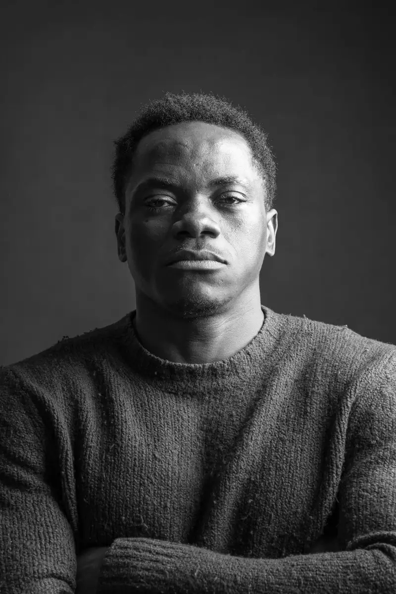 Black-and-white portrait of a man with crossed arms in a knitted sweater, looking straight into the camera