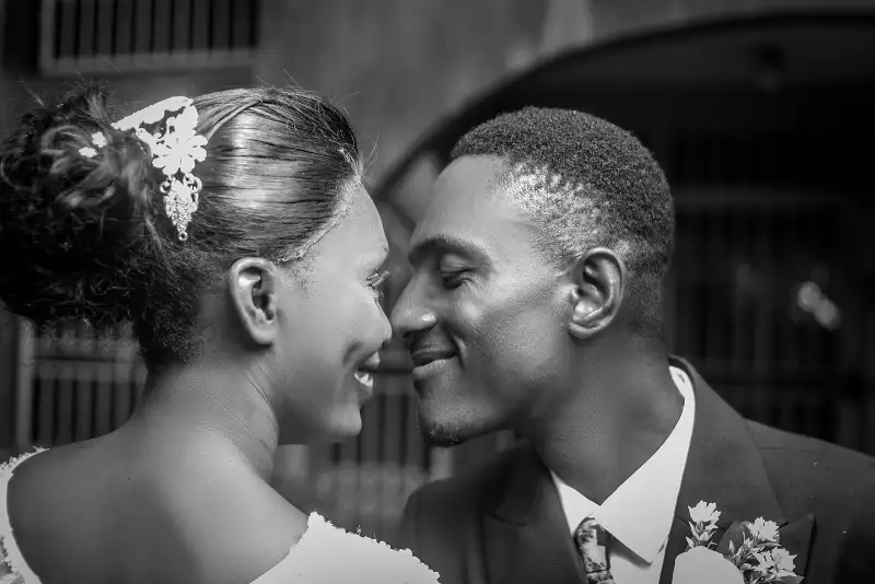 Black-and-white close-up of a bride and groom about to kiss, foreheads touching
