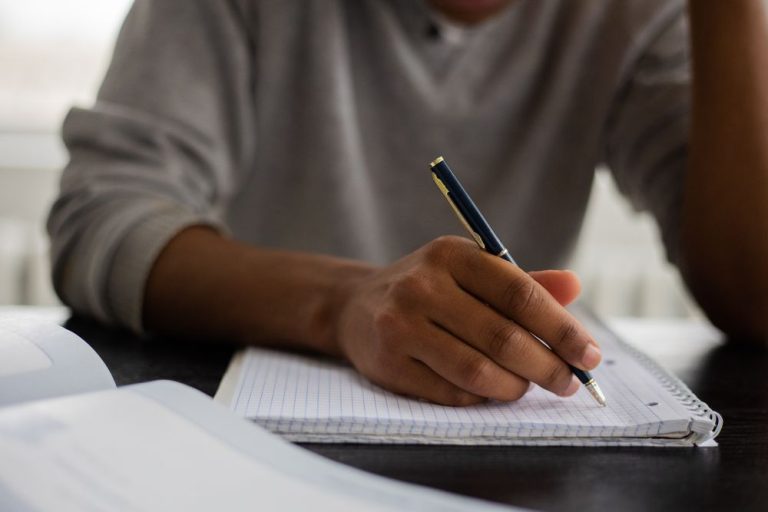 Hands writing notes in a notebook at a desk