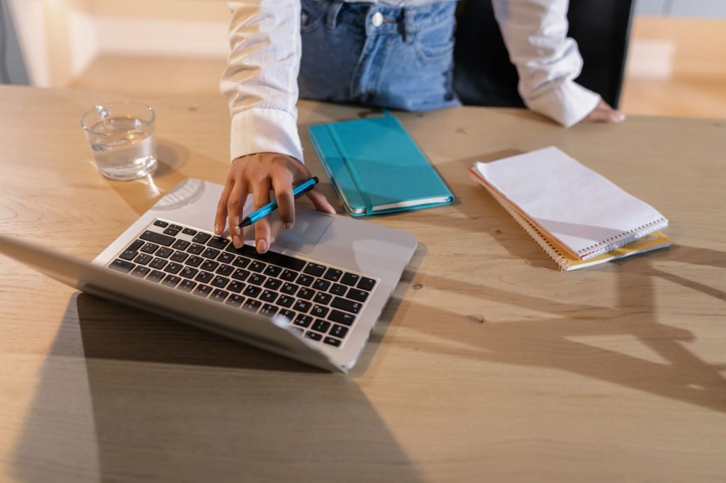 A laptop, notebooks and a glass of water on a wooden desk