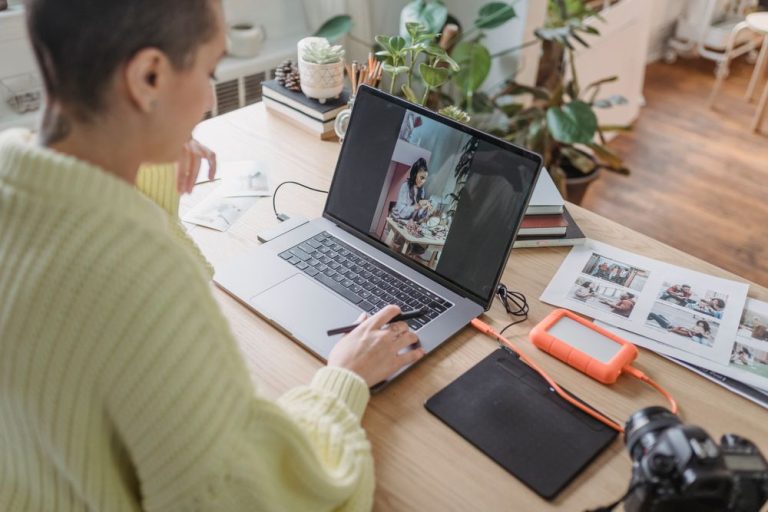 A woman editing photographs on a laptop at a desk with prints