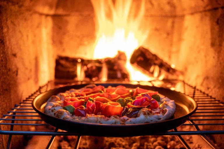 A pizza baking on a grate inside a wood-fired oven with flames behind it
