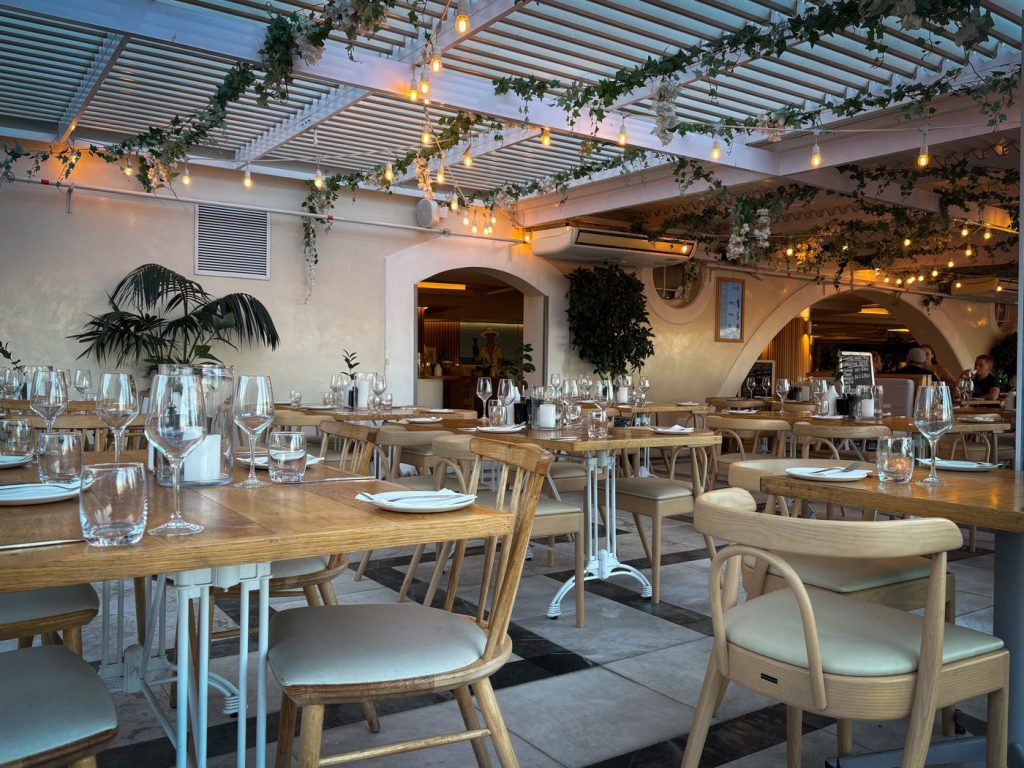 A bright dining room with wooden tables, chairs and string lights overhead