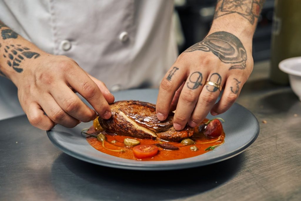 A chef's hands arranging a dish on a plate in a restaurant kitchen