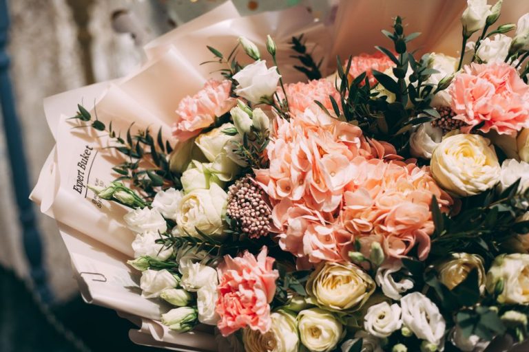 A hand-tied bouquet of peach roses and carnations wrapped in paper