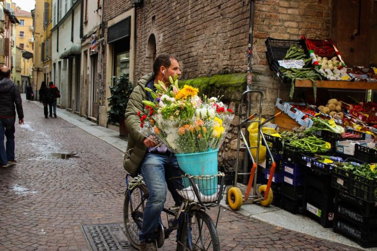 A cyclist delivering a basket of fresh flowers along a cobbled street