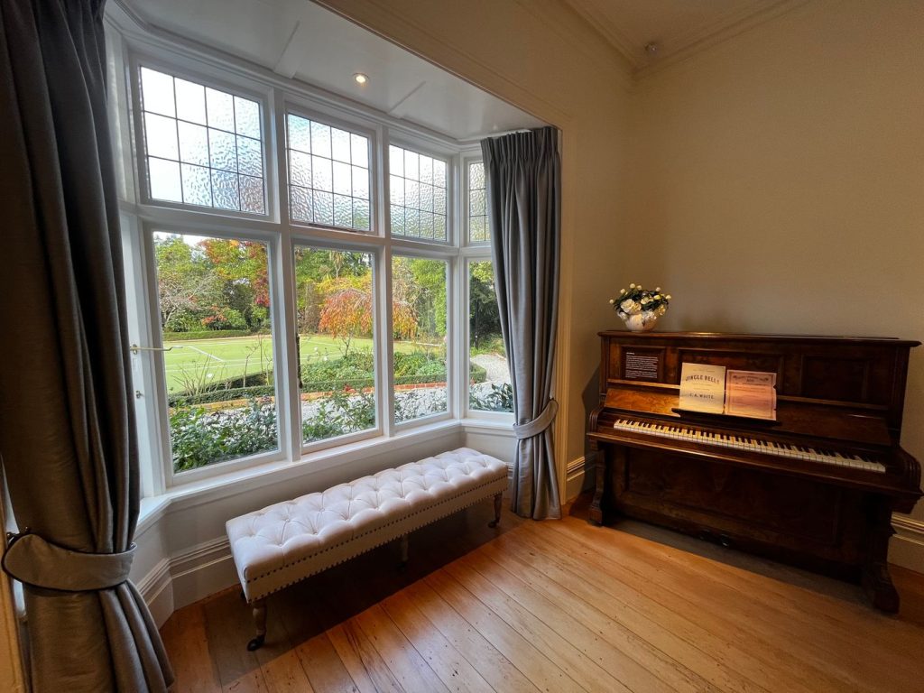 A music room with an upright piano beside a bay window
