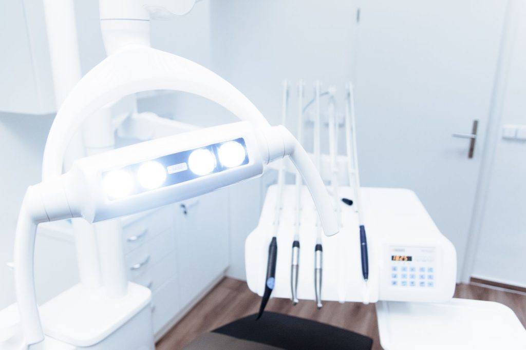 A bright dental treatment room with an overhead light and a white chair