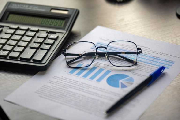 A calculator, reading glasses and printed charts on a desk