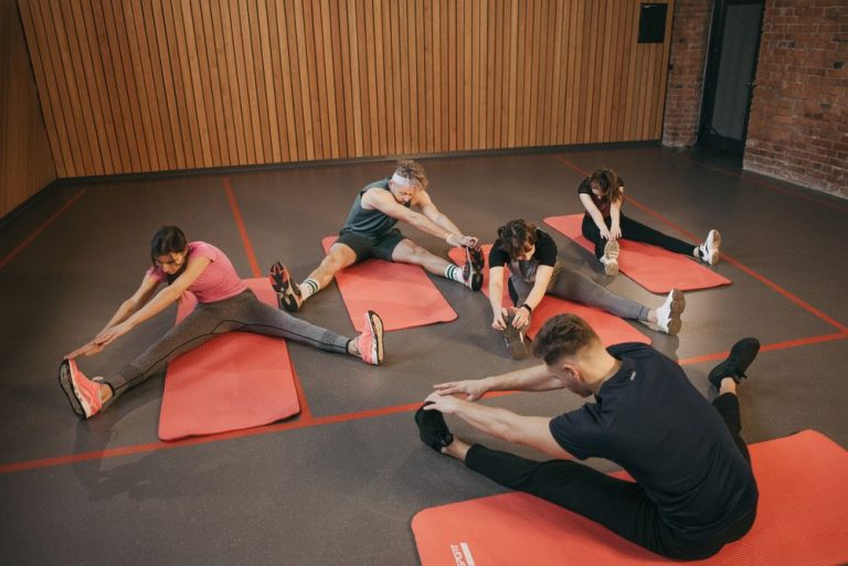 A group class stretching on mats in a gym with warm wooden walls