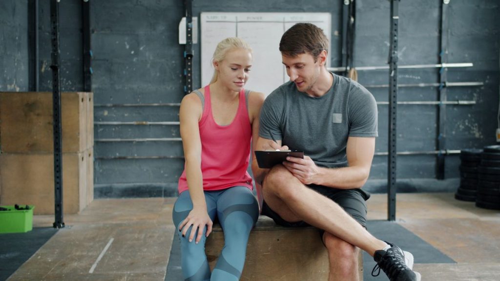 A coach and a client reviewing a plan on a tablet in a gym