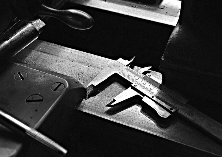 A precision caliper measuring a metal part, in black and white