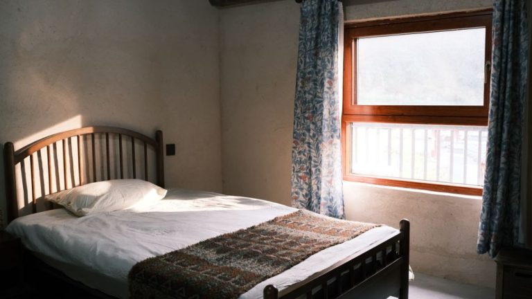 A simple bed made up with white linen beside a window