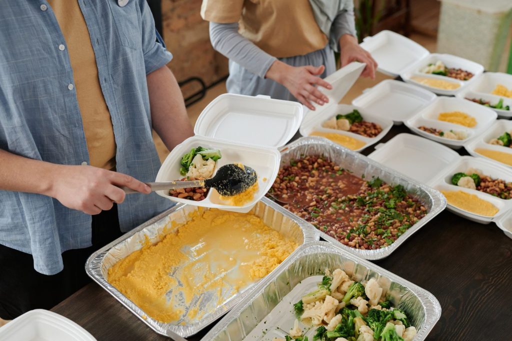 Volunteers portioning hot meals into containers on a long table