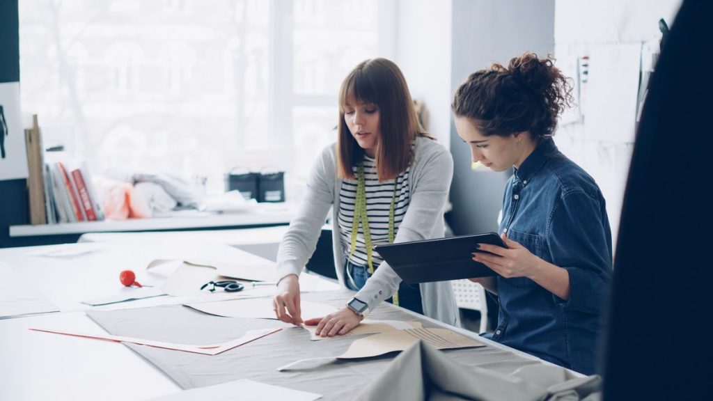 Two designers reviewing drawings together on a tablet at a bright studio table