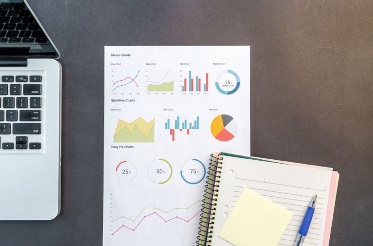 Printed charts and a notebook on a desk beside a laptop