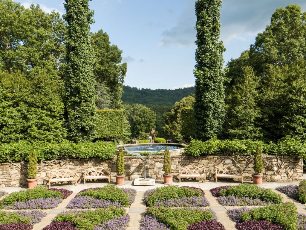 A formal garden with symmetrical planting beds, clipped hedges and a stone bench