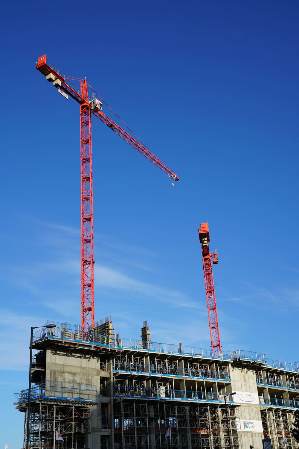 Two red tower cranes above a concrete-framed building against a blue sky
