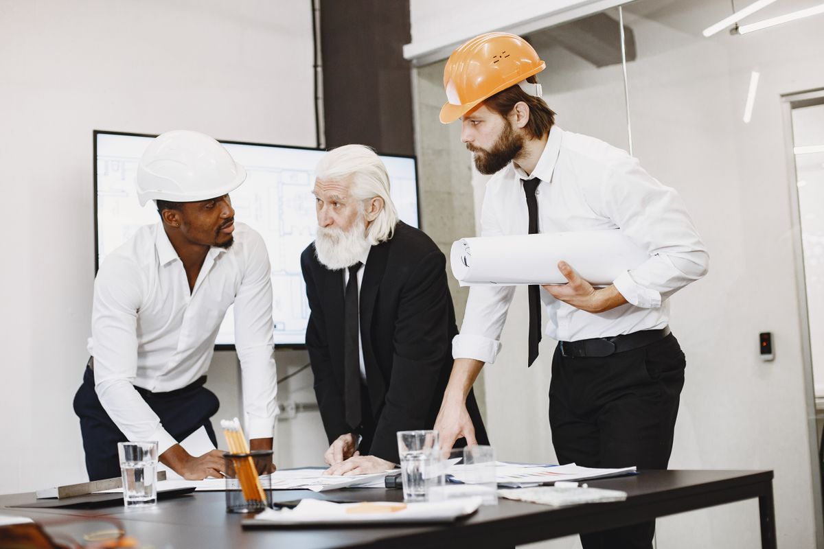 Three colleagues in white shirts reviewing architectural plans around a table