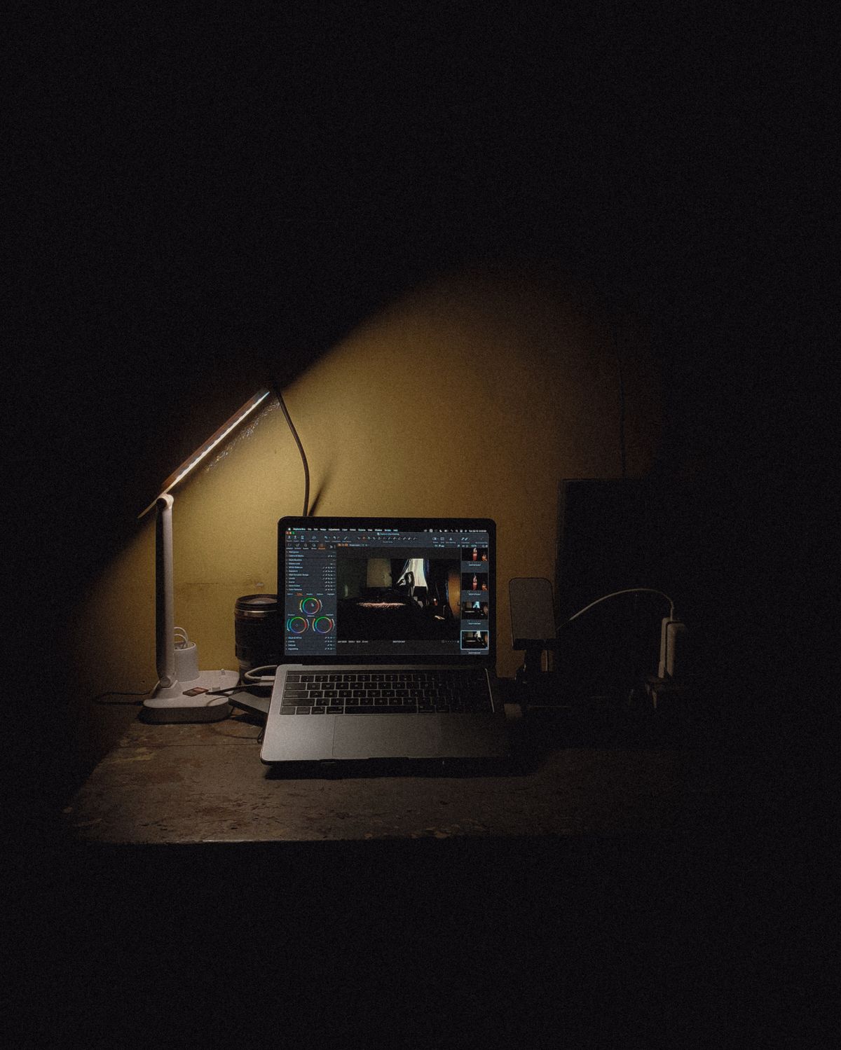 A laptop glowing on a dark desk under a warm desk lamp
