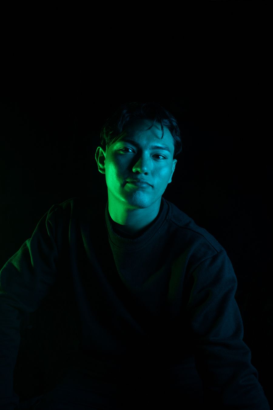 A young man lit by green and blue light in a dark room