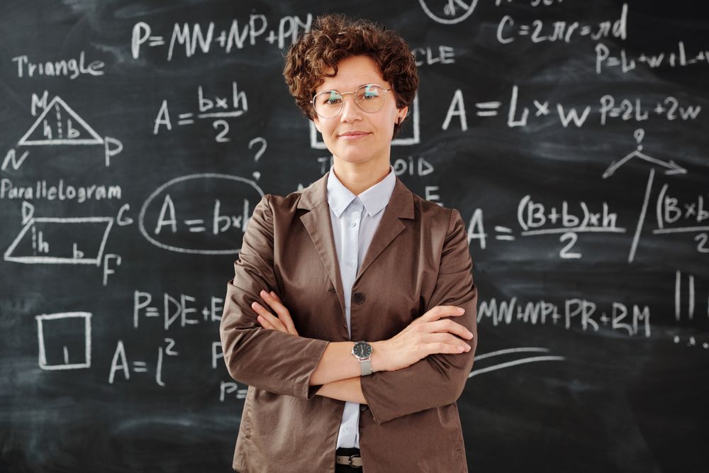 Dr Maya Levin standing with folded arms in front of a chalkboard of geometry
