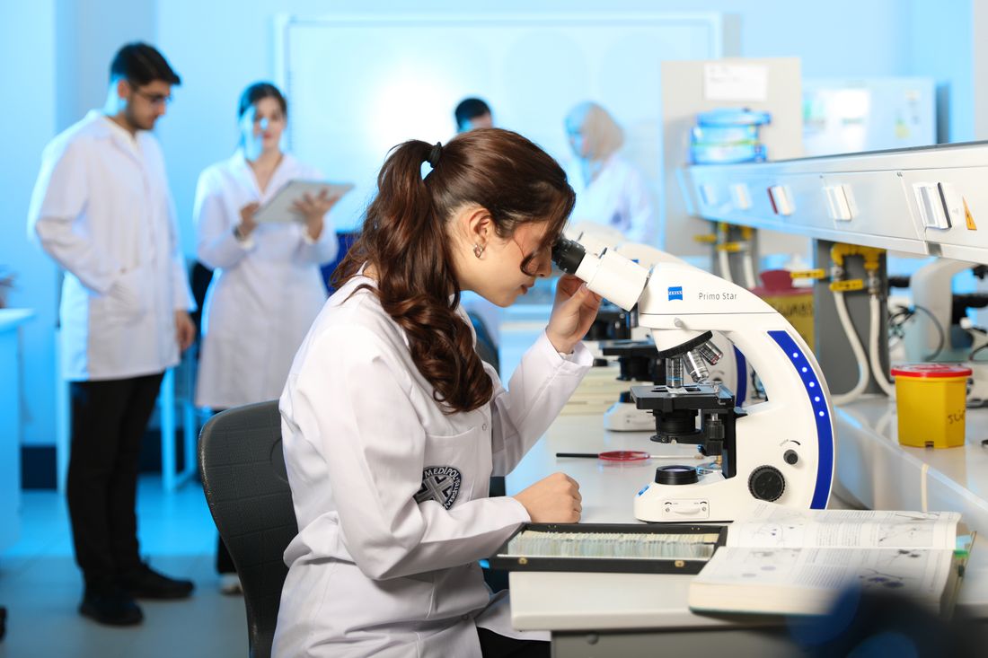 A student in a lab coat looking through a microscope in a laboratory