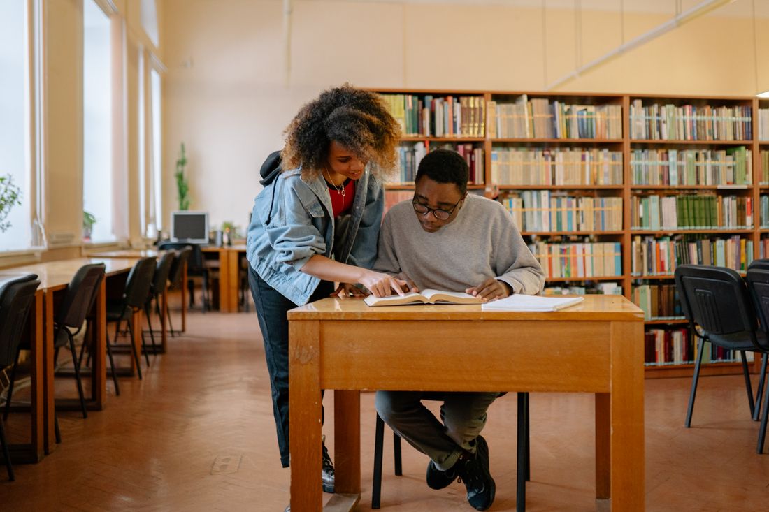 Two students working together at a wooden table in a library
