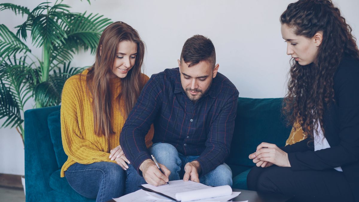 A young couple signing a financial agreement with an adviser on a sofa