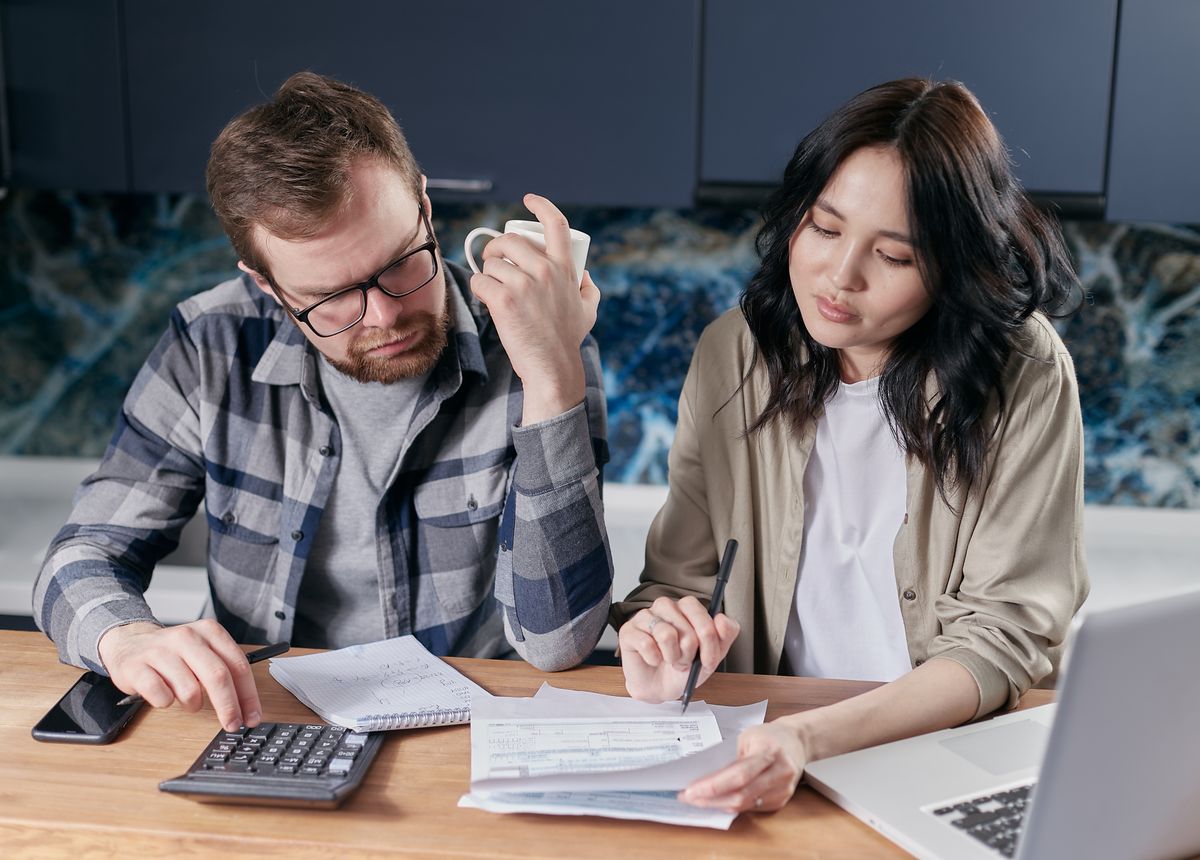 A couple reviewing household paperwork and a calculator with a laptop
