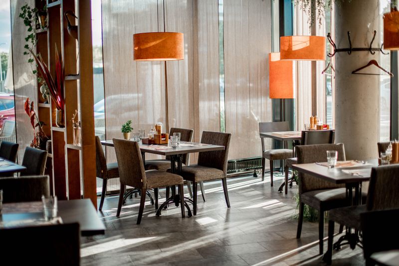 A bright dining room with wooden tables and orange pendant lamps