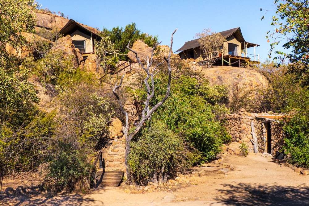 Two safari tents built onto a granite outcrop among low trees
