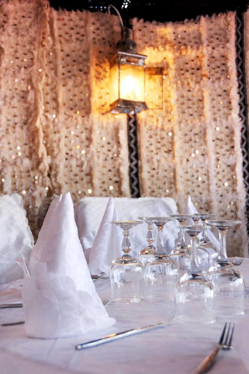 A dinner table set with glasses and folded napkins beside a lantern