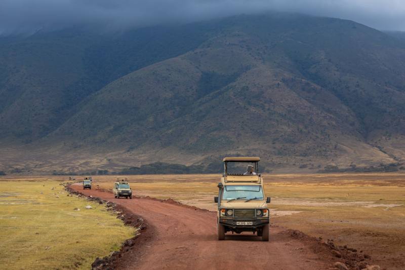 Safari vehicles on a red dirt road below a range of hills