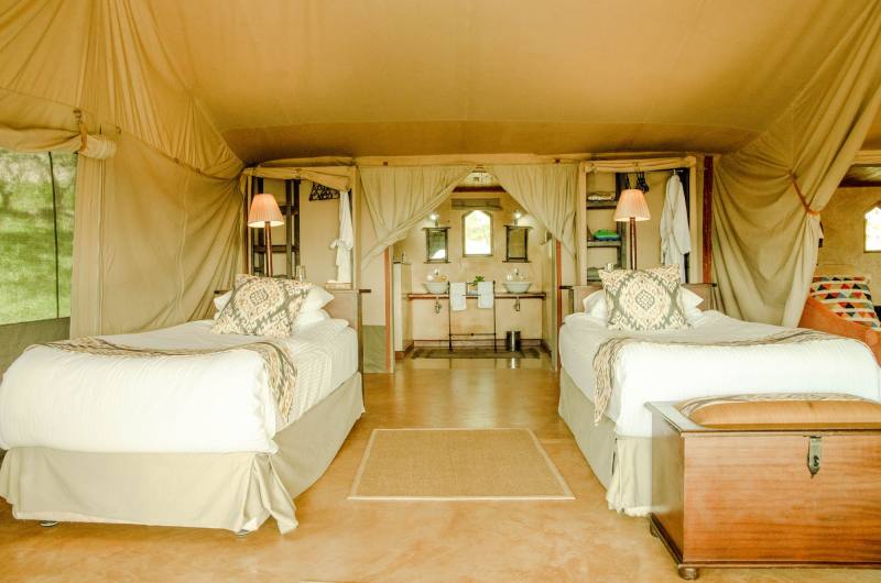 Inside a canvas tent with two beds, a wooden chest and soft lamps