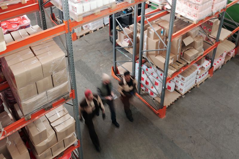 Warehouse workers moving between orange racking stacked with boxes, seen from above