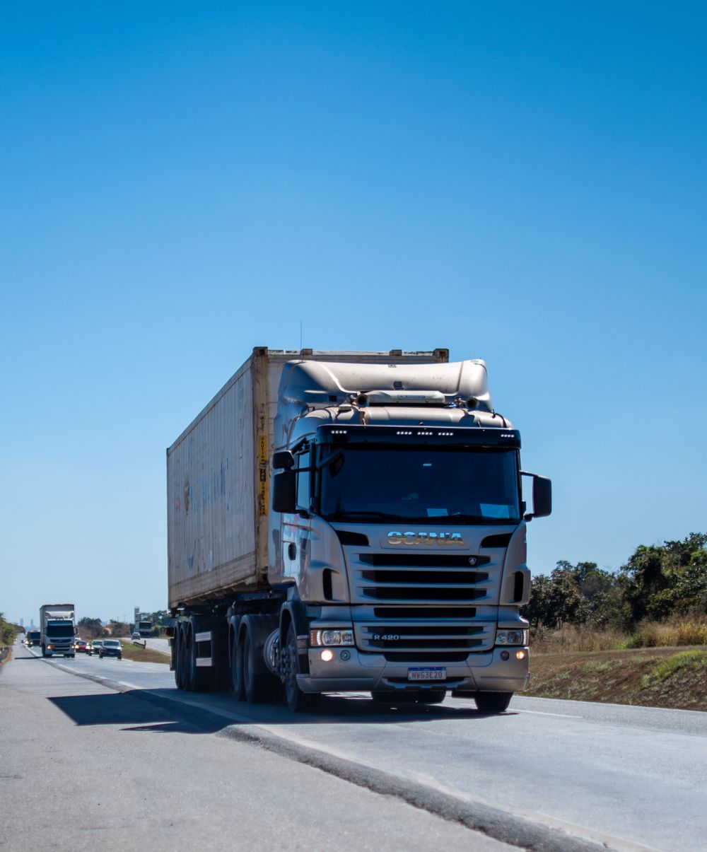 A blue freight truck with a trailer driving along a sunny road