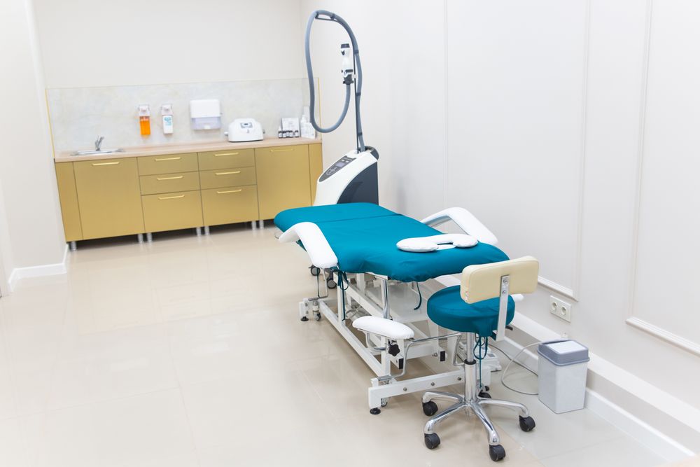 A bright physiotherapy treatment room with a teal treatment couch