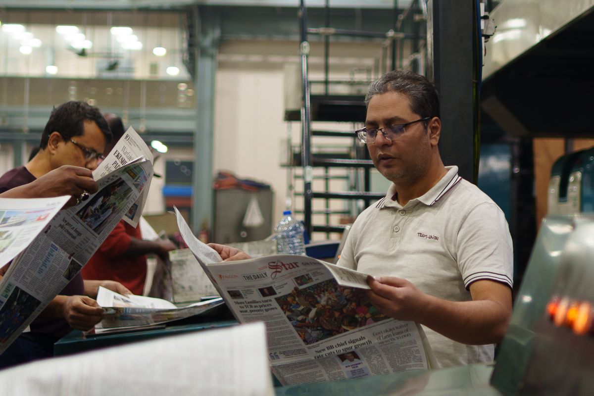 Print workers reading newspapers off the press at a printing factory