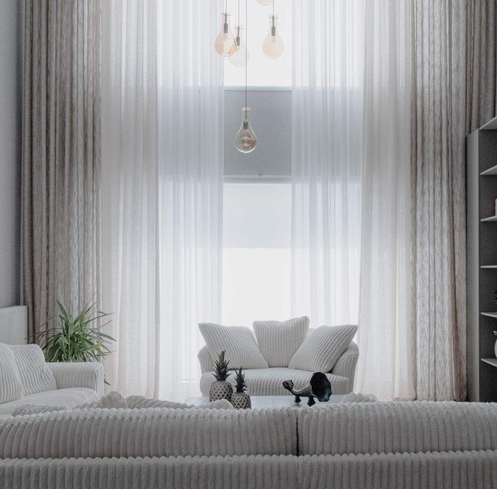 A bright living room with soft white sofas and tall sheer curtains