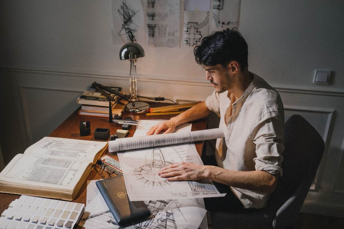 A designer at a desk working over large drawings and books