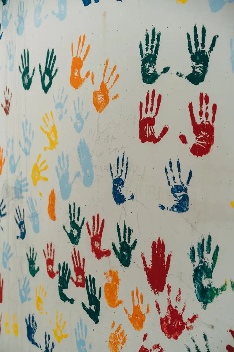 A white wall covered in painted handprints in red, blue, green, yellow and orange