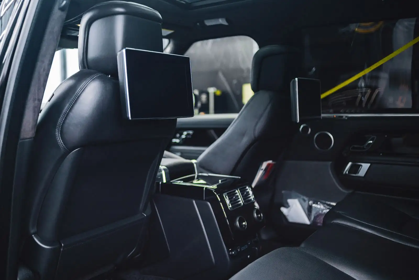 The rear seats of a luxury saloon in black leather, each with a screen in the back of the front headrest