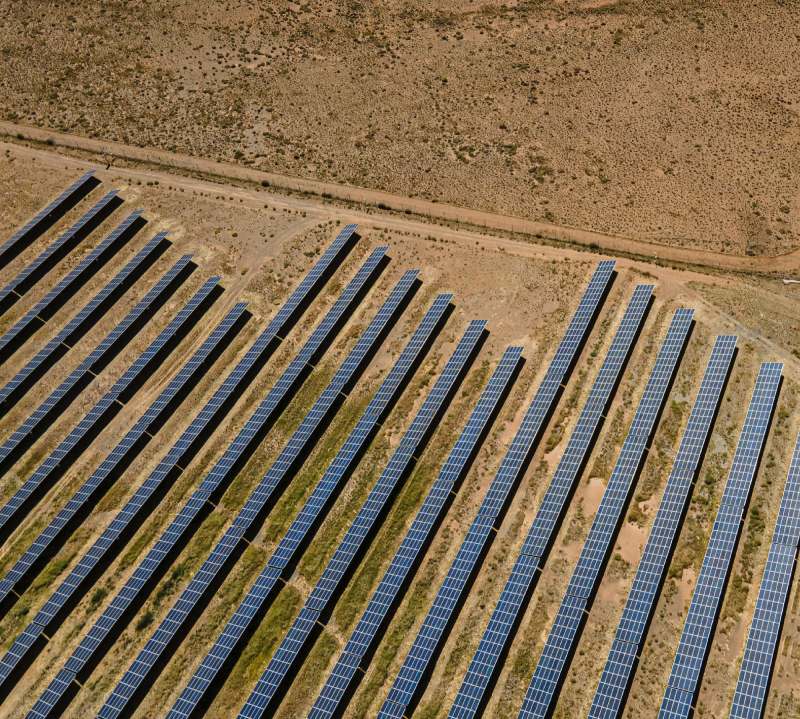 An aerial view of rows of ground-mounted solar panels on dry land